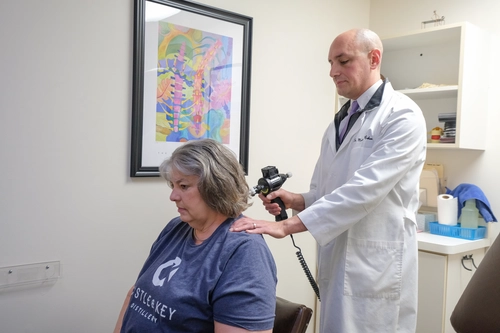 Chiropractor using a muscle stimulation device on a patient's neck